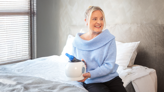 A woman sitting on a bed with the WellO2 breathing trainer