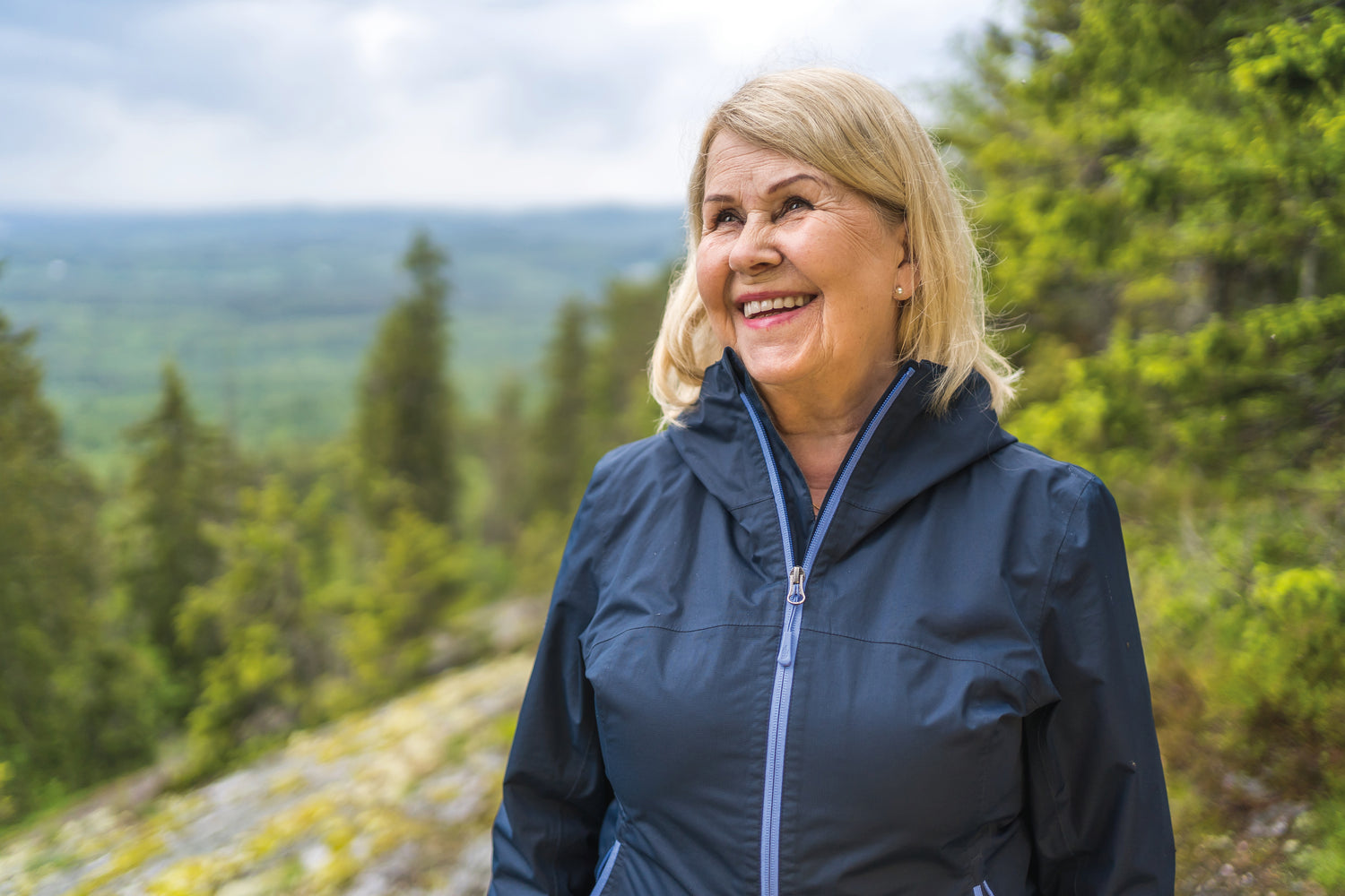 Woman in a blue jacket standing in a forested area in Finland with a scenic background
