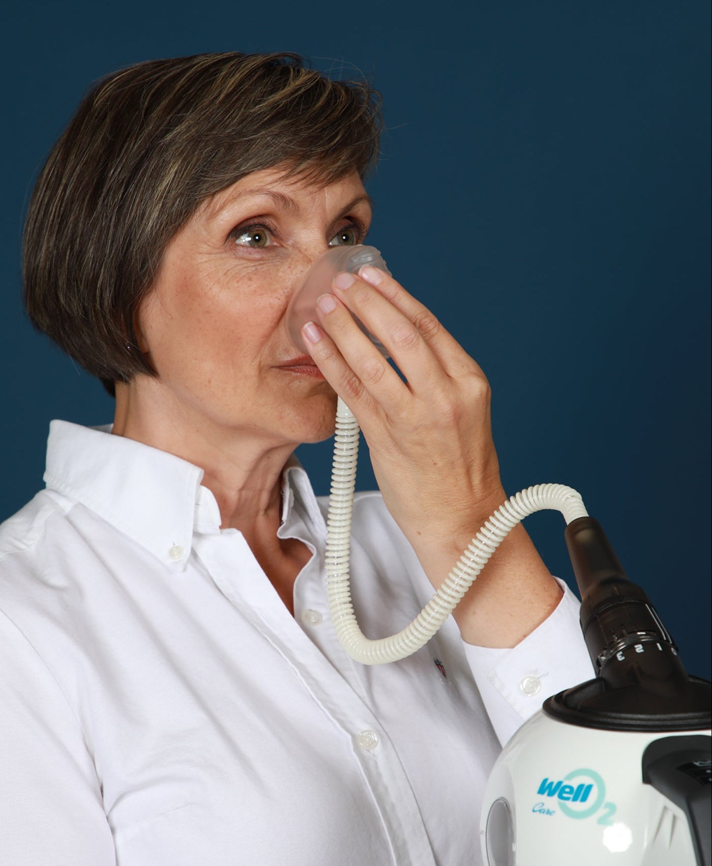 Woman using a WellO2 steam breathing trainer with nasal mask against a blue background